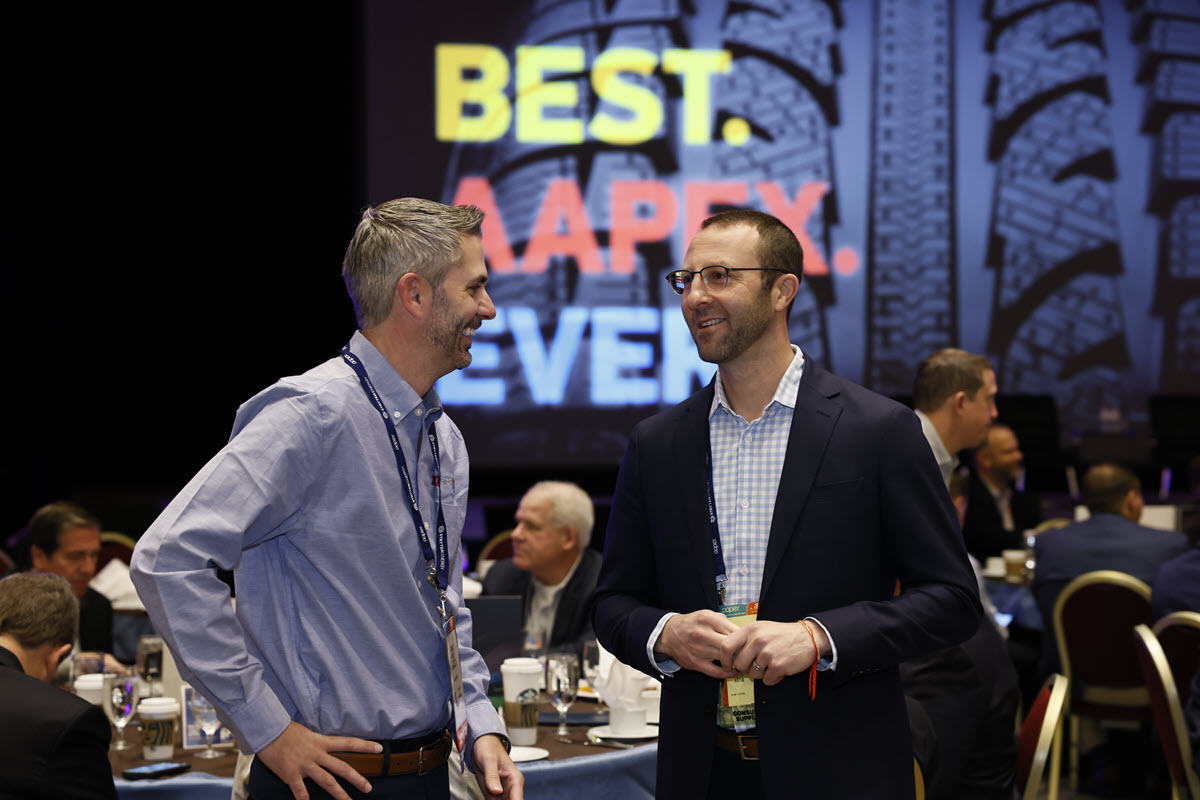 Two attendees talk at a breakfast session in front of a Best AAPEX Ever screen