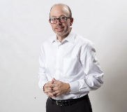 Photo of Mick Nardelli wearing black pants, a white shirt, with his hands clasped